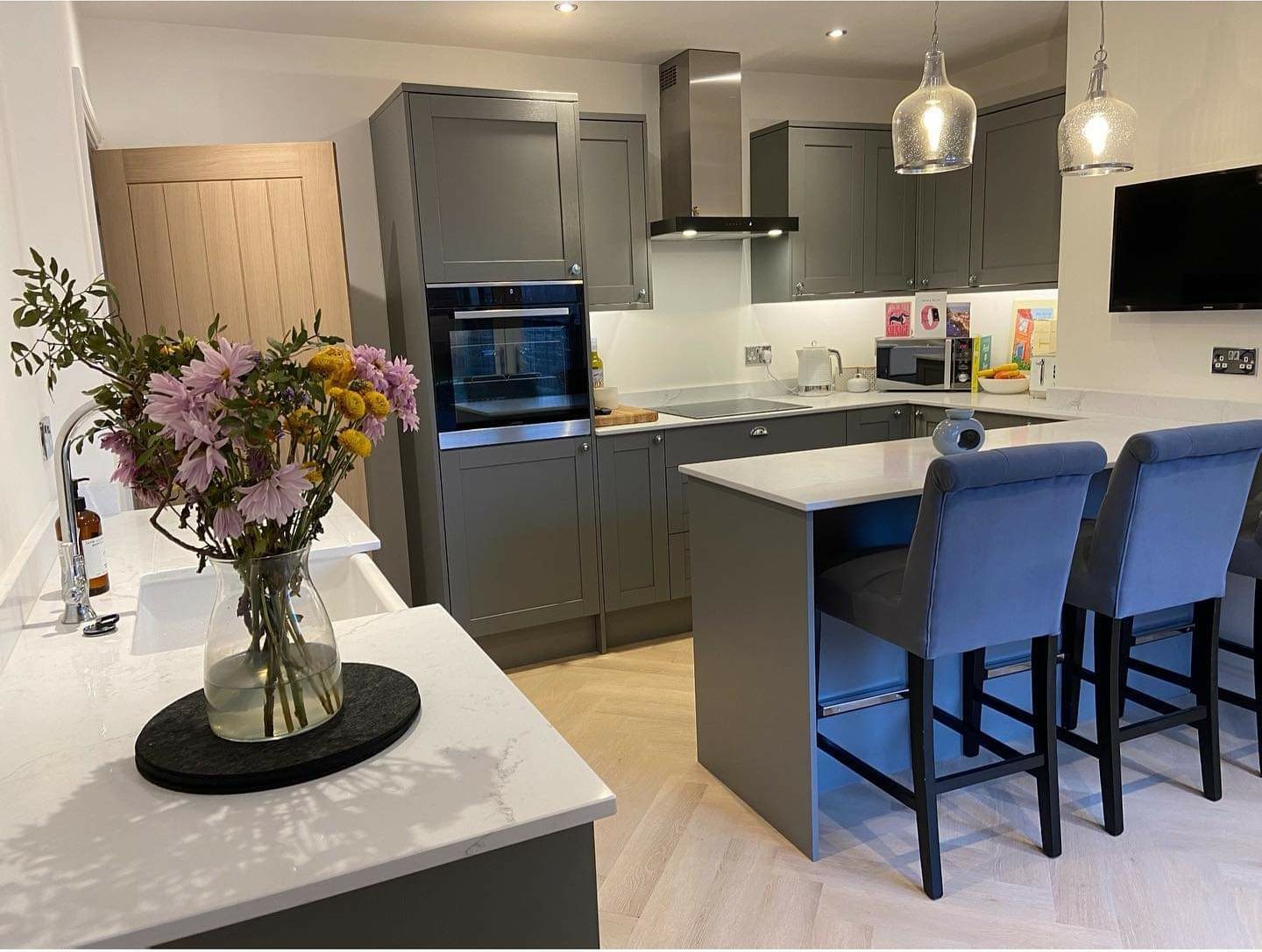 A dark grey fitted kitchen with a white worktop breakfast bar and an oak door